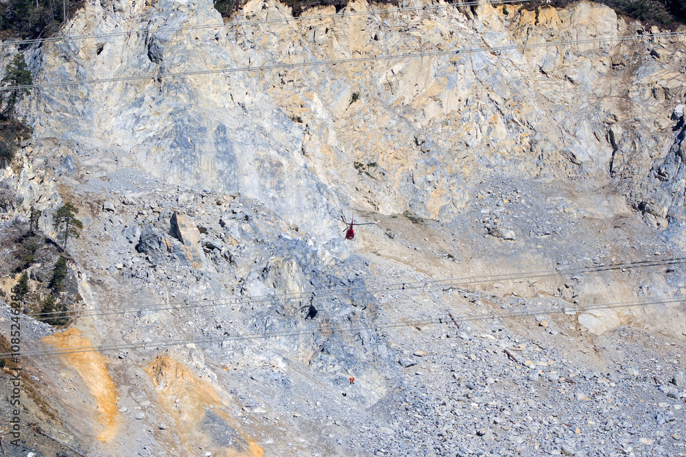 Fototapeta premium Rockfall at mountain village of Brienz Brinzauls with helicopter and workers hanging on rope in the Swiss Alps on a sunny autumn day. Photo taken November 15th, 2024, Brienz Brinzauls, Switzerland.