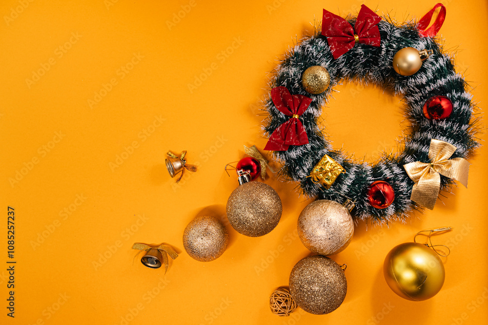 Holiday decoration featuring a Christmas wreath with ornaments and bows, creating a cheerful contrast on an orange surface. Holiday decoration featuring a Christmas wreath with ornaments and bows, creating a cheerful contrast on an orange surface.