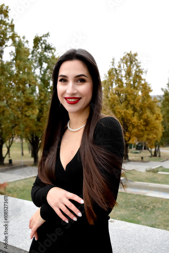 A beautiful woman in a black dress and red lipstick walks through the autumn city. Concept of style, fashion and professional makeup.