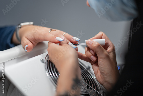 Beautiful professional woman manicurist doing manicure and painting nails with brush in beauty salon