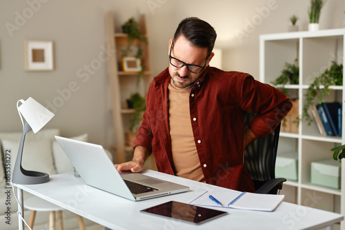 Man working from home suffering backache while using laptop