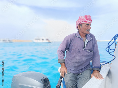 Old Sailor in the Sea Riding and Sailing with his Boat An old sailor with a white with a white mustache who is wearing a Bedouin Scarf on his head