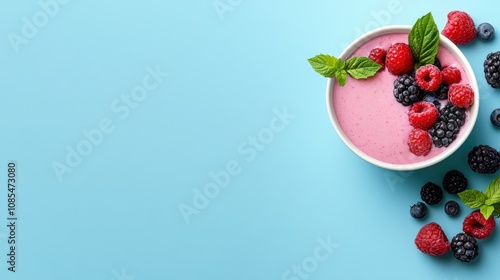 A vibrant smoothie bowl topped with fresh raspberries, blackberries, and mint leaves against a light blue background.