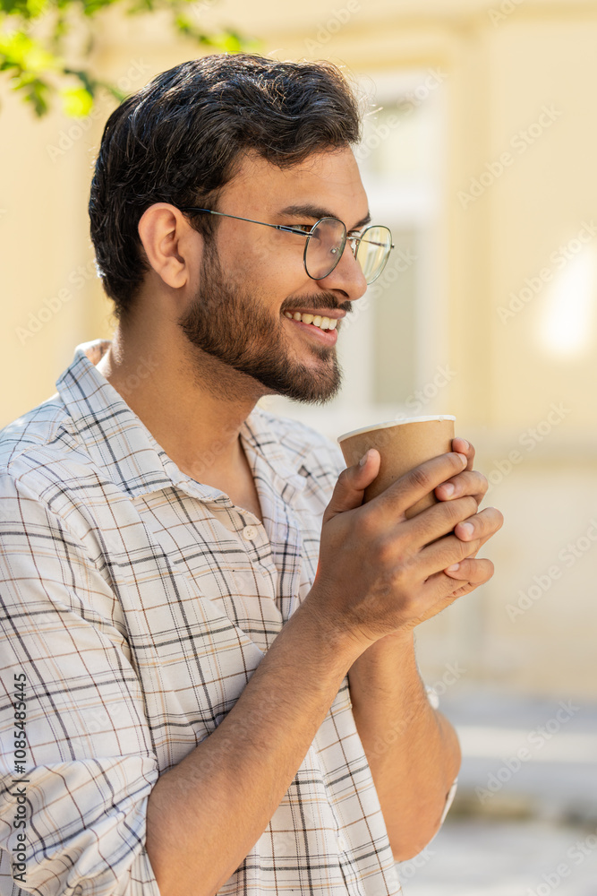 Happy Indian man enjoying morning coffee hot drink and smiling. Relaxing, taking a break. Hispanic young guy standing on urban city center street, drinking coffee to go. Town lifestyles outside. Happy Indian man enjoying morning coffee hot drink and smiling. Relaxing, taking a break. Hispanic young guy standing on urban city center street, drinking coffee to go. Town lifestyles outside.