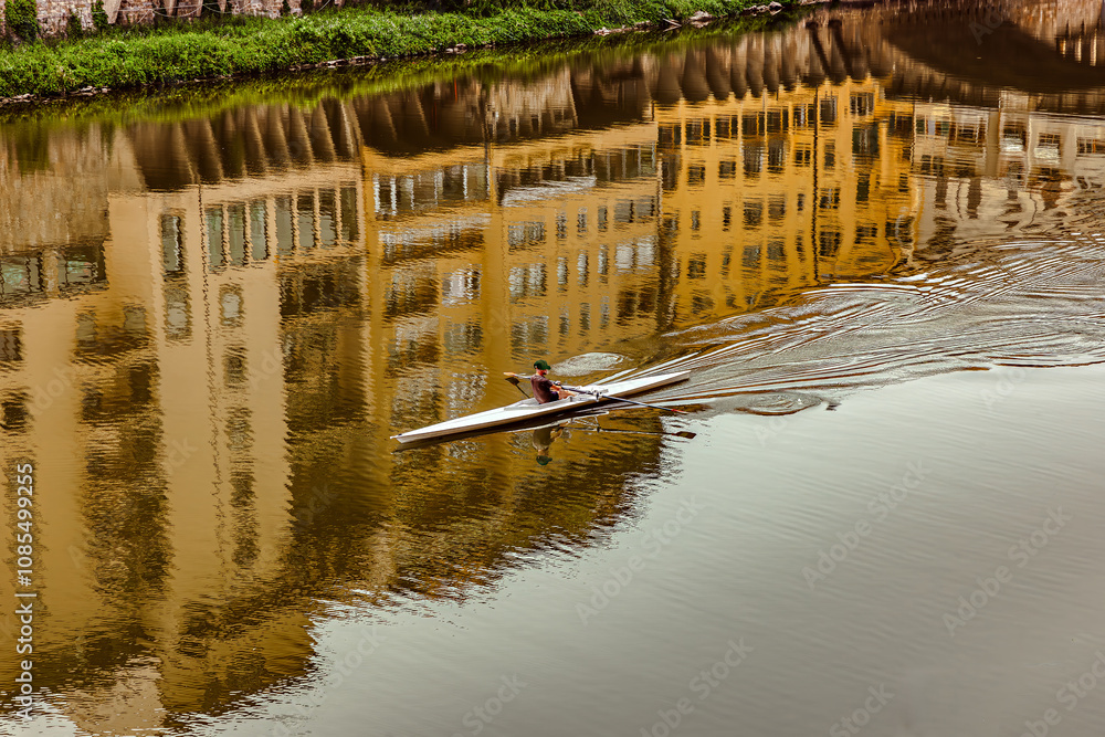 A lone kayaker navigates the serene waters of the Arno River, showcasing the beautiful reflections of historic Florence buildings against a clear sky.