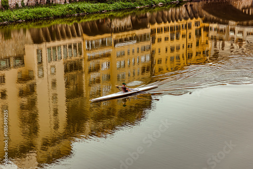 Obraz na płótnie A lone kayaker navigates the serene waters of the Arno River, showcasing the beautiful reflections of historic Florence buildings against a clear sky. w salonie