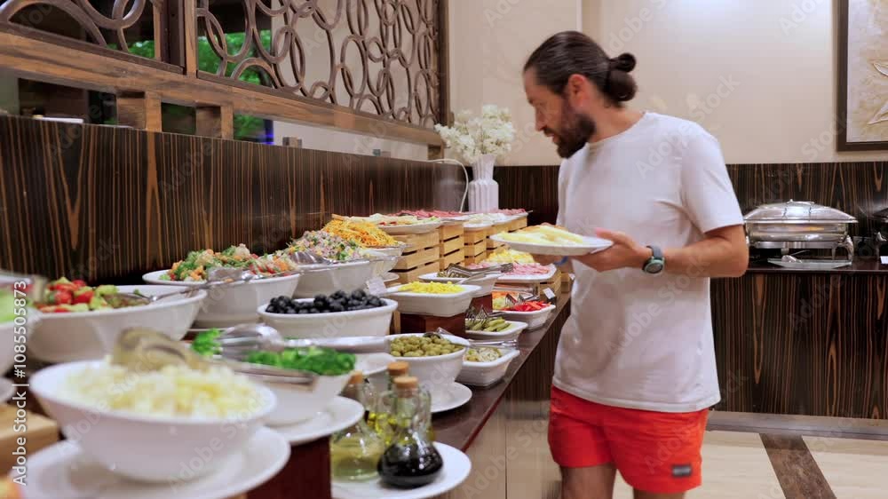 A man chooses food at a hotel restaurant for breakfast in a self-service setting. This video showcases the abundance of delicious breakfast options available for guests A man chooses food at a hotel restaurant for breakfast in a self-service setting. This video showcases the abundance of delicious breakfast options available for guests