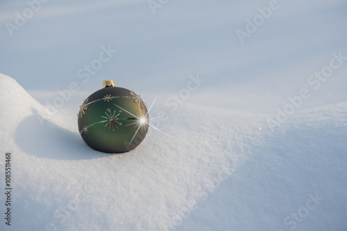 A green bauble with gold decorations lying on white natural snow  with star on a sunny frosty day.