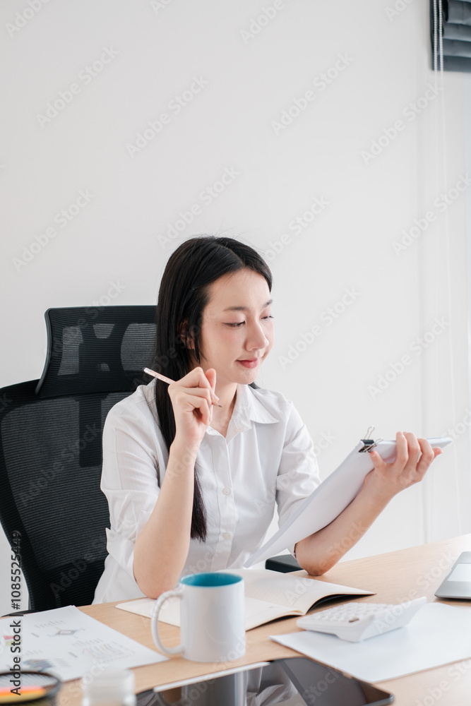 Young Professional Woman Analyzing Documents in Modern Office Setting with Pen and Clipboard Young Professional Woman Analyzing Documents in Modern Office Setting with Pen and Clipboard