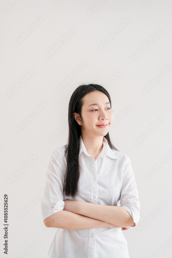Confident Young Woman in White Shirt Posing Against Minimalist White Background with Arms Crossed and a Calm Expression Confident Young Woman in White Shirt Posing Against Minimalist White Background with Arms Crossed and a Calm Expression