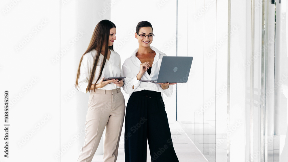 Two business women in the lobby of a modern office are discussing the work of a new project. Business, technology and teamwork concept. Two business women in the lobby of a modern office are discussing the work of a new project. Business, technology and teamwork concept.