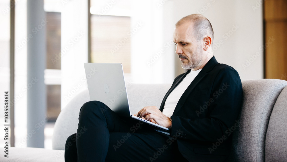 Businessman uses laptop computer in office lobby. Middle-aged man, entrepreneur, small business owner, working online at a laptop. Businessman uses laptop computer in office lobby. Middle-aged man, entrepreneur, small business owner, working online at a laptop.