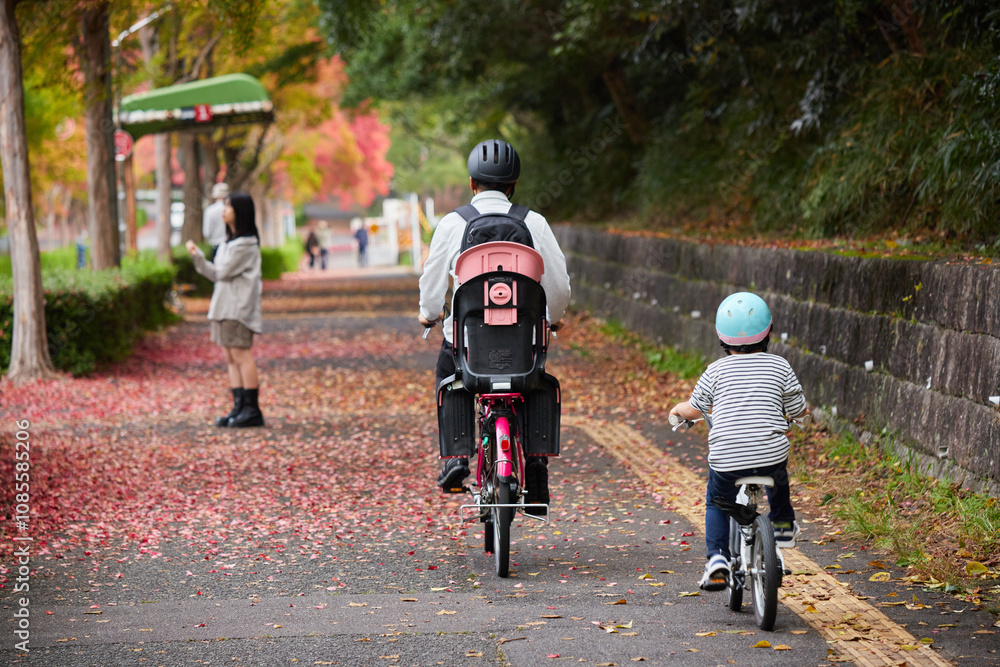 Obraz premium 秋の公園の赤色の紅葉の落ち葉の風景と自転車を乗る親子の姿