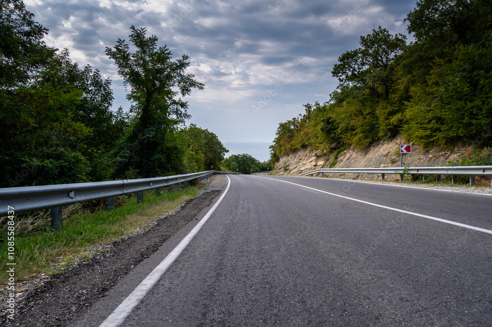 Road landscape forest, mountains and sea on the horizon. Empty long mountain road to the horizon on a sunny summer day with dramatic cloudy sky. Highway turn panoramic view. Road landscape forest, mountains and sea on the horizon. Empty long mountain road to the horizon on a sunny summer day with dramatic cloudy sky. Highway turn panoramic view.