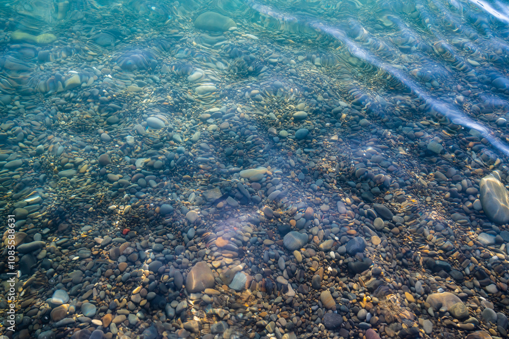 Underwater pebble backgrounds. Colorful stones sea bottom in the sun rays. View from above through clear water. Seascape wallpaper texture. Soft focus.