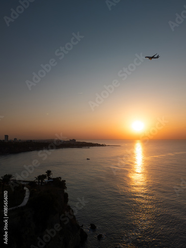 Tranquil coastal landscape at sunrise, featuring a cascading waterfall flowing gently into the calm sea. Warm golden hues of the rising sun reflect on the water, plane is flying