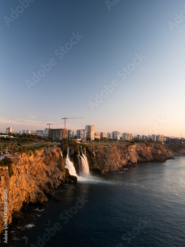 Tranquil coastal landscape at sunrise, featuring a cascading waterfall flowing gently into the calm sea. Warm golden hues of the rising sun reflect on the water