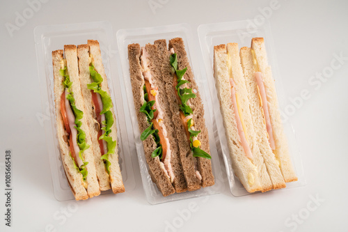 Three packaged sandwiches with white and whole wheat bread, filled with lettuce, tomatoes, turkey, cheese, ham and greens. Ideal for quick meals.