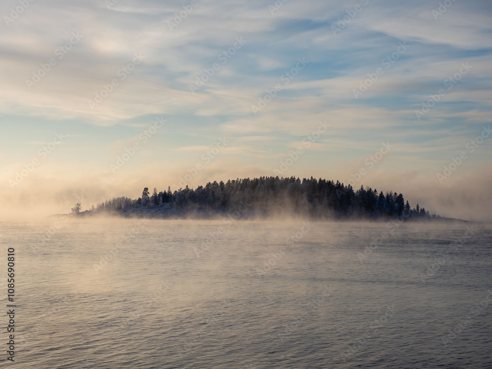 Fog over the water of Lake Ladoga in the Republic of Karelia in severe frost, view of the island on a sunny day Fog over the water of Lake Ladoga in the Republic of Karelia in severe frost, view of the island on a sunny day