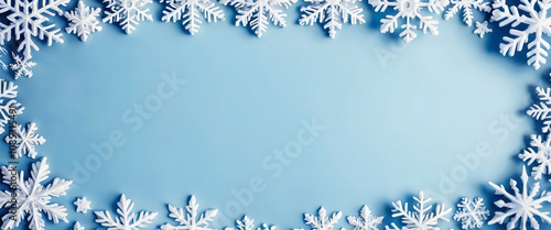 Snowflakes of different sizes and shapes creating a winter frame on a light blue background with a brighter central area. Christmas template.