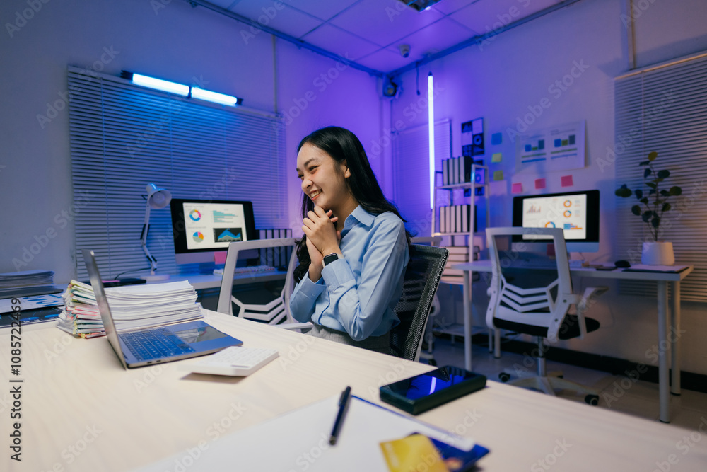 Happy young asian businesswoman looking at laptop and celebrating success, working late at night in modern office with blue and purple neon light Happy young asian businesswoman looking at laptop and celebrating success, working late at night in modern office with blue and purple neon light