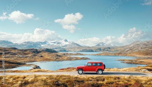 A red vehicle parked by a serene lake, surrounded by mountains under a clear blue sky.