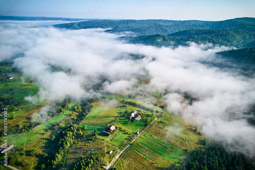 Aerial view of dense forest partially shrouded in mist, revealing patches of vibrant green trees. Fog gradually unveils quaint village nestled among trees, creating serene and enchanting landscape. Aerial view of dense forest partially shrouded in mist, revealing patches of vibrant green trees. Fog gradually unveils quaint village nestled among trees, creating serene and enchanting landscape.