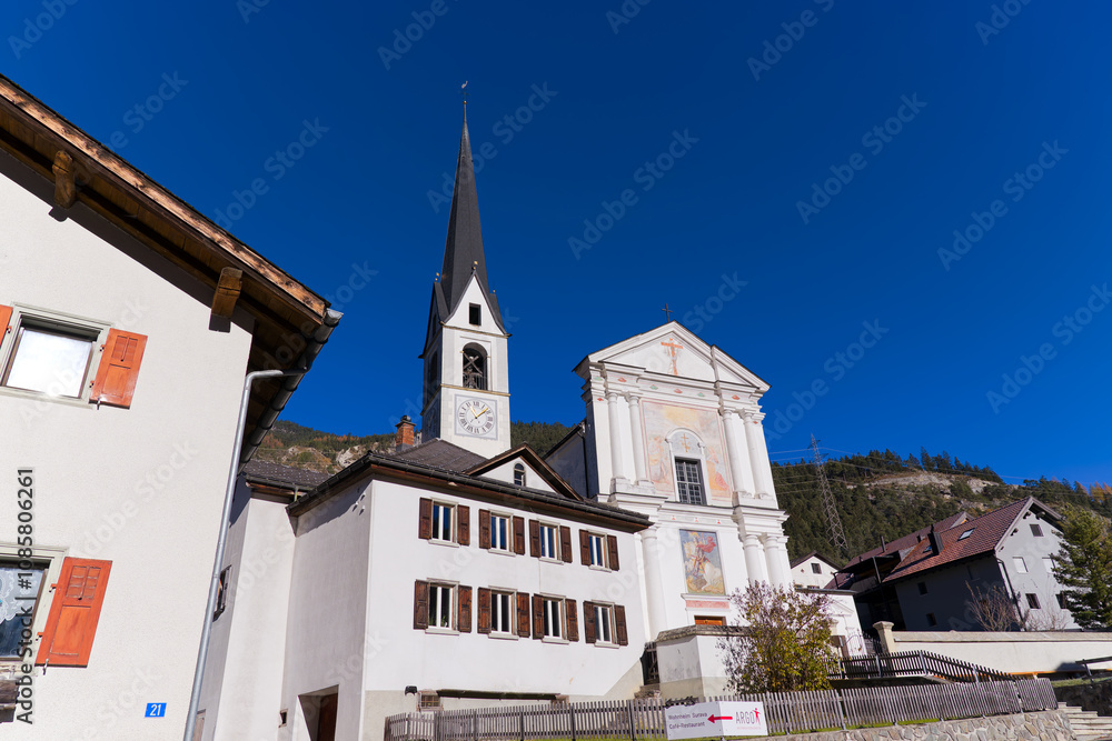 Fototapeta premium Looking up to church surrounded by houses at Swiss mountain village of Surava on a sunny autumn day. Photo taken November 15th, 2024, Surava, Switzerland.