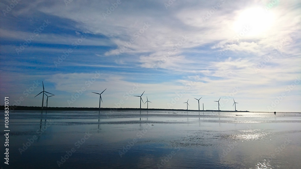 Taichung, Taiwan - 8.12.2018: Wind turbines standing along the edge of Gaomei Wetlands under a blue sky near sunset in the summer with tourists far away Taichung, Taiwan - 8.12.2018: Wind turbines standing along the edge of Gaomei Wetlands under a blue sky near sunset in the summer with tourists far away