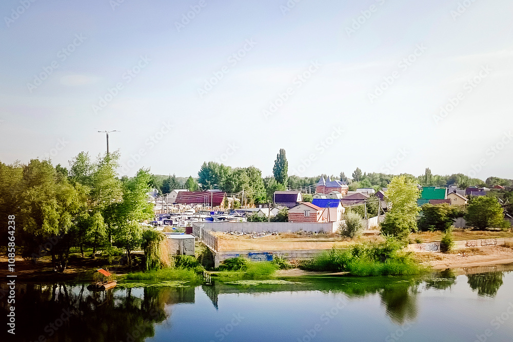 Fototapeta premium Small summer cottages among green trees on the bank of a clean river.