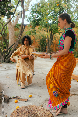 Indian musician in traditional clothes playing sitar festive season outdoor home. Woman in traditional saree hand lighting Diya lamp during Diwali festival. Happy greeting photo. Part of a series