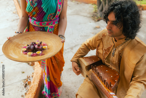 Indian musician in traditional clothes playing sitar festive season outdoor home. Woman in traditional saree hand lighting Diya lamp during Diwali festival. Happy greeting photo. Part of a series