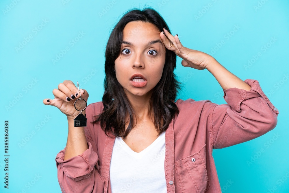 Young hispanic woman holding home keys isolated on blue background with surprise expression Young hispanic woman holding home keys isolated on blue background with surprise expression