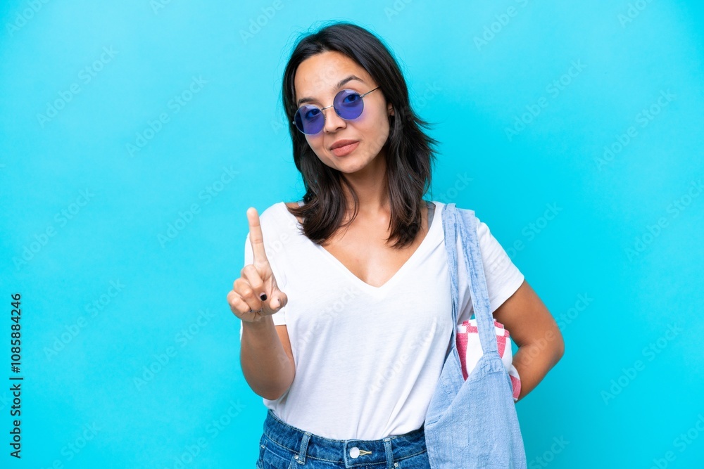 Fototapeta premium Young caucasian woman holding a beach bag isolated on blue background showing and lifting a finger