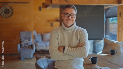 Portrait of successful mature manager wearing turtleneck sweater and smart watch, enjoying winter vacation in beautiful chalet. Happy mid adult man with grey hair and glasses smiling to camera.