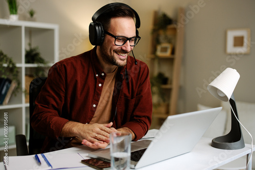 Happy businessman wearing headphones and working from his home office having a video conference on his laptop