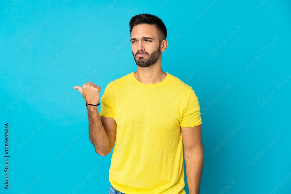 Young caucasian man isolated on blue background unhappy and pointing to the side Young caucasian man isolated on blue background unhappy and pointing to the side