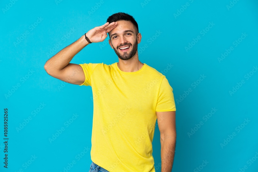 Young caucasian man isolated on blue background saluting with hand with happy expression Young caucasian man isolated on blue background saluting with hand with happy expression