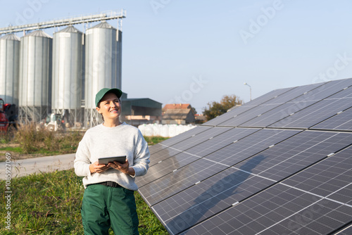 Female farmer with digital tablet on a modern farm using solar panels. Agricultural silos in the background. photo