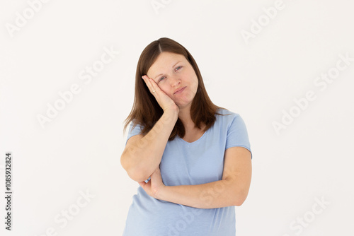 Cute redhead woman standing in blue t-shirt, holding palm on cheek and leaning face on it, being bored and tired of uninteresting talks over white wall