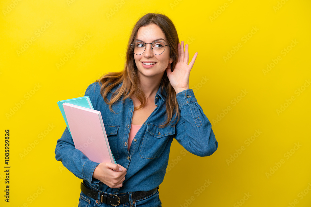 Young student caucasian woman isolated on yellow background listening to something by putting hand on the ear Young student caucasian woman isolated on yellow background listening to something by putting hand on the ear