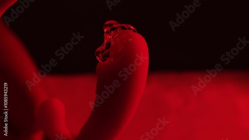 A woman holds adult toys and a condom in her hand on a white blanket in a bedroom.