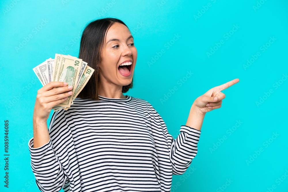 Young caucasian woman taking a lot of money isolated on blue background pointing finger to the side and presenting a product Young caucasian woman taking a lot of money isolated on blue background pointing finger to the side and presenting a product