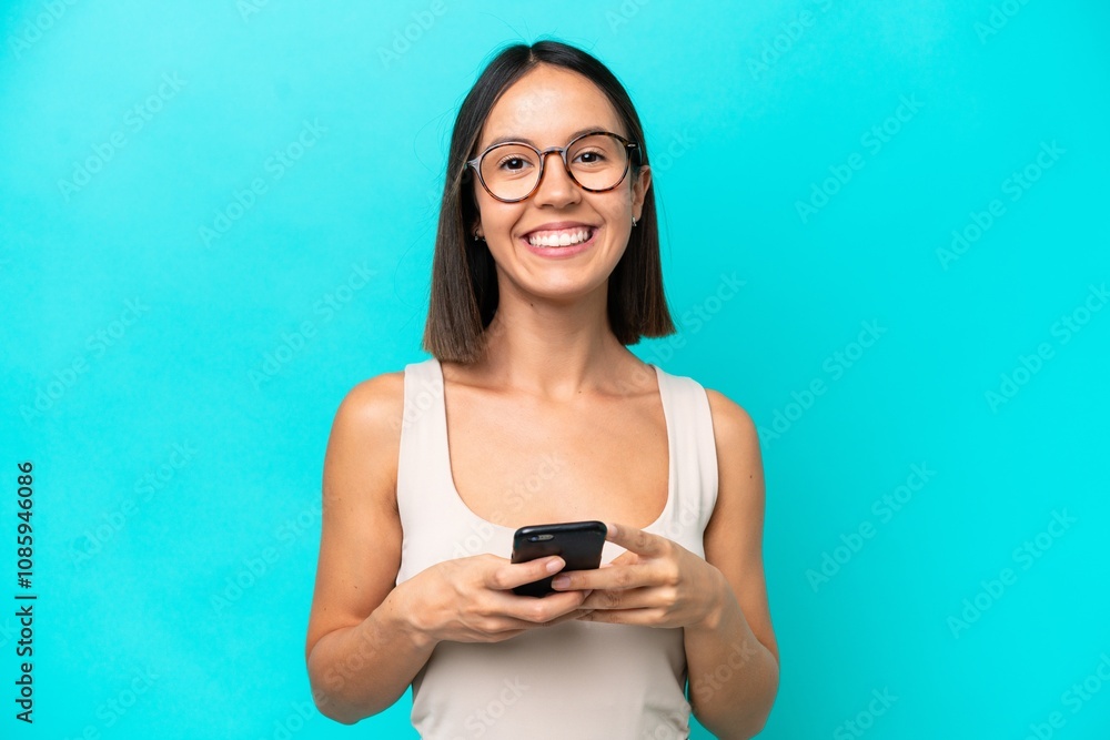 Young caucasian woman isolated on blue background looking at the camera and smiling while using the mobile Young caucasian woman isolated on blue background looking at the camera and smiling while using the mobile