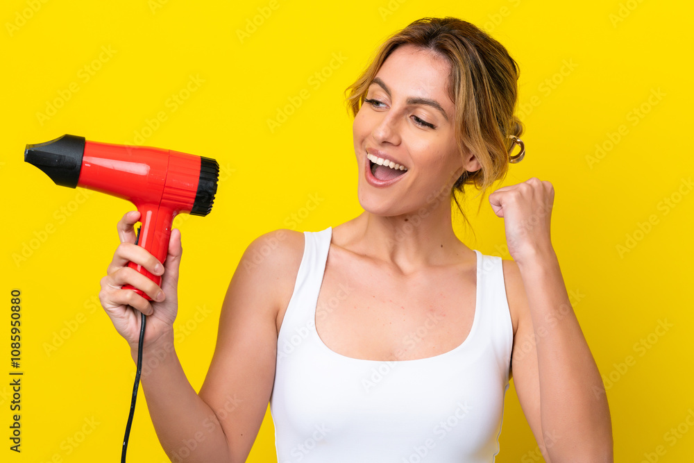 Young Uruguayan woman holding a hairdryer isolate don yellow background celebrating a victory Young Uruguayan woman holding a hairdryer isolate don yellow background celebrating a victory