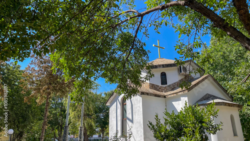 White Orthodox church surrounded by lush greenery under a clear blue sky, representing faith and peace. Suitable for religious events, travel campaigns, or cultural heritage promotions.