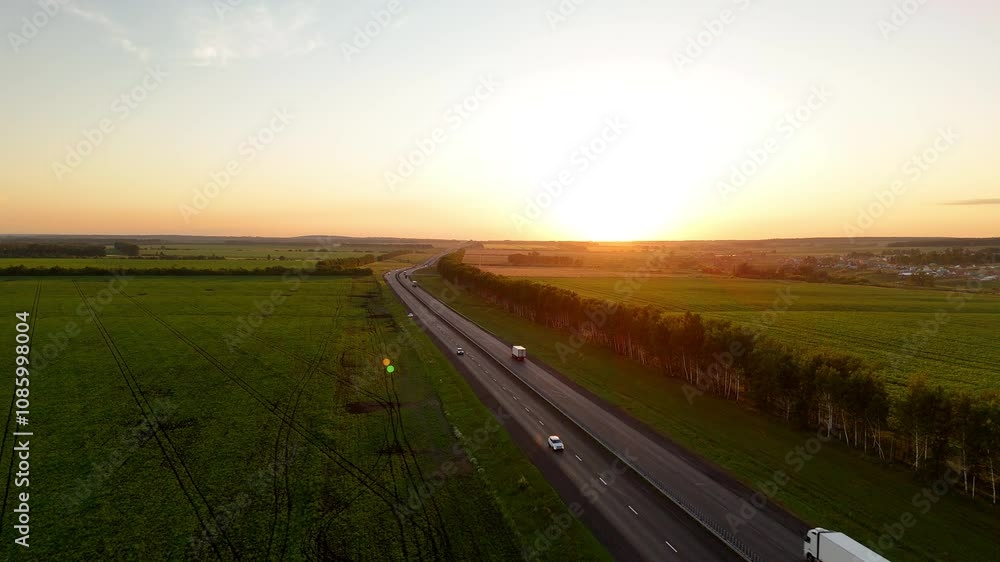Drone view of the highway in the rays of the setting sun and a moving truck with a semi-trailer. Heavy truck driving on an asphalt road along green fields. Aerial shot Drone view of the highway in the rays of the setting sun and a moving truck with a semi-trailer. Heavy truck driving on an asphalt road along green fields. Aerial shot