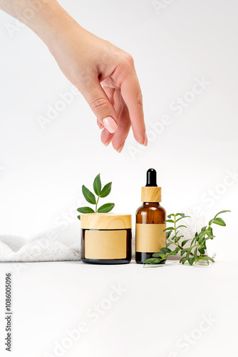 Hand Reaching for Amber Dropper Bottle with Skincare Jar photo