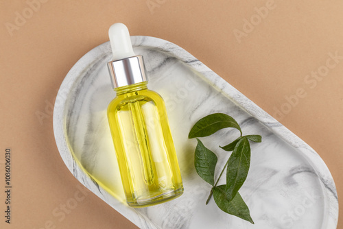 Elegant cosmetic dropper bottle on marble tray with leaf photo