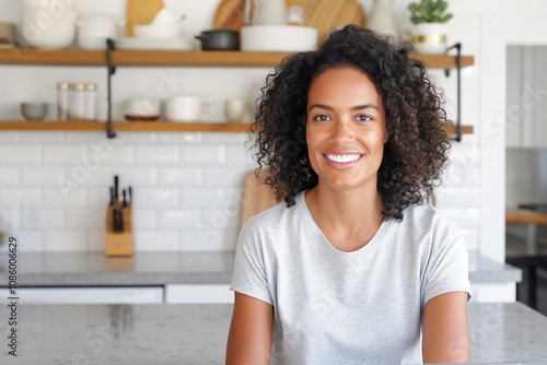 Cheerful Woman with curly hair enjoying moment in bright, minimalist kitchen. Great for themes of home comfort, lifestyle, and positivity.